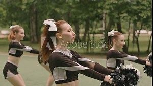 Group of young cheerleaders in sports uniform dancing with pom-poms and smiling while giving performance on outdoor soccer field