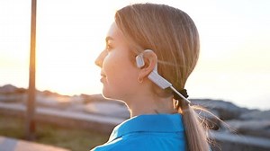positive young woman in bone conduction headphones in sunset