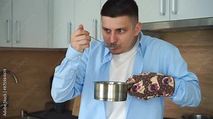 A man is preparing soup. Hot soup in a saucepan. A man tests his food for salt. A man holds a saucepan with an oven mitt. Hot dishes, fire, gas, stove