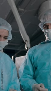 Two professional surgeons in robes, masks and disposable hats and gloves preparing equipment for serious surgery Vertical shot.