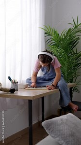 Little girl drawing sitting on a desk beside the window while listening to music on headphones.