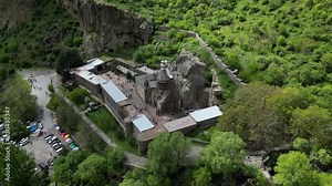 4K drone video of Geghard Monastery in Armenia. Zoom out shot from above. The church is located in a green valley with beautiful rock formations and its a sunny day.