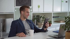 Young man smiling and gesticulate. Male talking with friend uses earphones.In the modern office shelves with folders