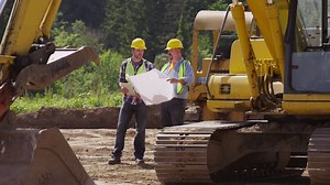 Download Two workers by excavation equipment look at blueprints for free