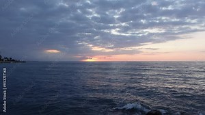 Timelapse of awesome sunrise between clouds at blue hour over water of the Mediterranean sea horizon. Clouds in sky and ocean waves moving fast