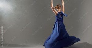 graceful ballerina in elegant blue dress spinning in dance. Young woman solo performing classic ballet dance. Beautiful young girl performs in studio, raising arms