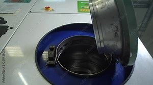 Low angle view of female worker hand opening laundromat before loading clothes for dry cleaning in salon. Close-up of big industrial laundry machine opened by dry-cleaning employee