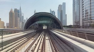DUBAI, UAE - July 2021. The subway train rides among the glass skyscrapers in Dubai, UAE.The electric train moving outside, driving into a dark tunnel. Planned change of lighting. Unmanned train. View