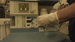 Anaesthetist preparing drug syringe in front of anaesthetic machine workstation for patient with coronavirus in hospital