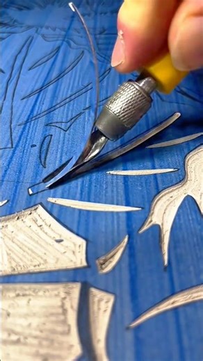Using a small V-gouge linocut tool to carve detailed patterns into a blue printing block