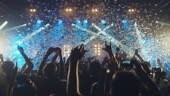 Crowd dancing and cheering at a concert while glitter is falling from...