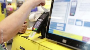 woman pays for purchases using a self-service machine with a touch screen scanning a barcode from a smartphone in a supermarket at the self-service checkout Payment by credit card through the terminal