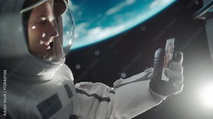 Young Astronaut Floating in Space in Zero Gravity. Spaceman Having a Video Call with a Young Female From Planet Earth. Engineer Using Smartphone in Open Space Outside an Orbiting Spacecraft