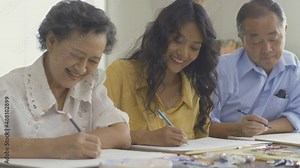 Young beautiful woman drawing pictures with senior people. She teaching her student to drawing picture at her class.
