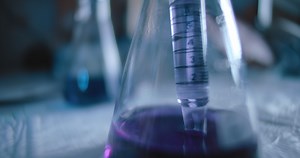 Scientist taking out a purple liquid from a conical flask in a lab