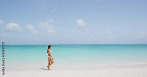 Beautiful woman in white bikini walking at beach. Young female is enjoying nature during her summer vacation. Scenic view of seascape against clear blue sky.