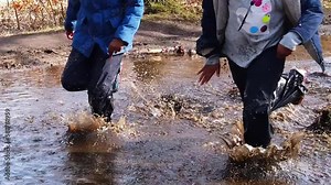Children, of African ethnicity, running and splashing in a large puddle of water for fun. Slow motion.