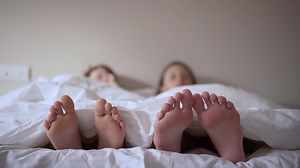 clip-1076307668-pair-feet-bed-on-white-sheets-child