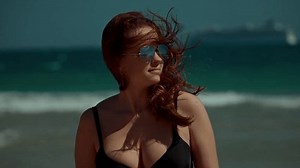 A captivating beach scene showcases a confident woman delighting in the waves while wearing stylish sunglasses