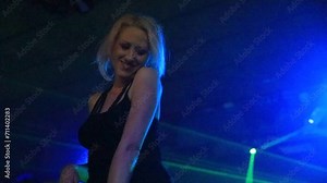 Dimly lit disco club, a beautiful woman is shown dancing to modern dance in slow motion under green strobe laser lights. Adult lifestyle scene in nightlife and entertainment.