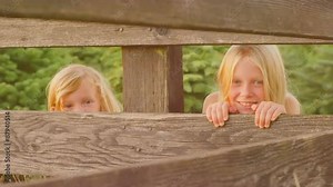 Young blonde girls peeking through a fence outside