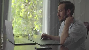 Confident bearded man draws using graphic tablet looking into a laptop. Male hand drawing 3d animation production modeling design modern coworking studio.