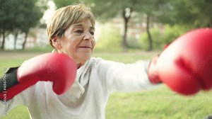 Senior woman doing boxing workout training with personal trainer outdoor