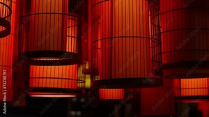 Lots of red paper lanterns in shape of cylinder put into metal cages hang on street and shine in the evening. Decorative lamps made in traditional Chinese style and often used for celebrating New Year