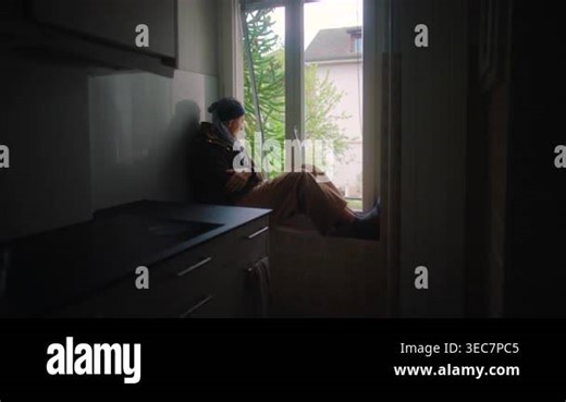 cancer patient sitting on kitchen window ledge at home looking outside reflecting on treatment journey recovery and mental strength during chemotherapy isolation and hope Stock Video Footage - Alamy