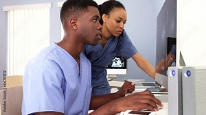 Two African American surgeons in blue scrubs working at computer stations