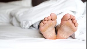 Delicate female feet moving toes playfully on white bedding