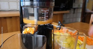 Man preparing fresh healthy juice with a juice extractor. Homemade apple, carrot, lemon, ginger recipe. Remains from slow cold press juicer. Kitchen background. 4K UHD 59.94fps ProRes 422 HQ 10 bit