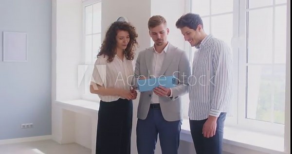 Agent greeting clients with handshake showing real estate contract. Inside a bright new home, realtor organizes signing and guides the buyer couple. Housing and property purchase agreement.