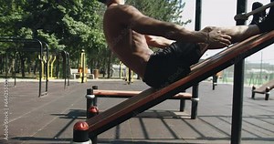 Athletic man doing sit up exercise on incline bench at gym outdoors. Sporty male has workout, training abs muscles and doing crunch with equipment