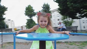 Happy little girl playing at playground, Pretty child laughing spinning on a carousel. Adorable girl has fun with parents on Merry Go Round in a city park.