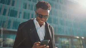 Portrait of cheerful man with smartphone in city street, good news and win. Happy black guy rejoicing by lottery win or successful business deal, reading messages in internet, modern urban landscape