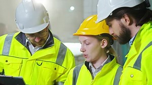 Close up of Caucasian team of builders at construction site talking and discussing work with tablet. Males and female co-workers at building. Constructors team. Constructing concept. Manufactory.