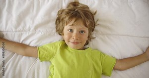 Boy sleep on the bed and open eyes with smile. Concept of joyful wake up