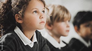 Schoolgirl sitting next to classmates, attentively watching and focused during class, showing concentration and engagement in the learning environment.