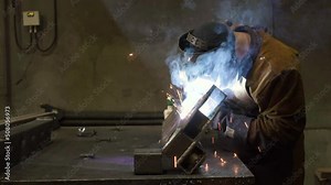 Close-up blacksmith welder in protective mask works with metal steel and iron using a welding machine, bright sparks and flashes. 4K flat footage