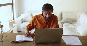 Serious focused middle-aged Portuguese man writing important information in personal organizer, take notes or to-do list in paper planner, make task sit at desk staring at computer screen. Workflow