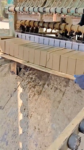 A row of freshly molded clay bricks is precisely cut and shaped by an automated brick-making machine