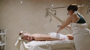 Masseuse massages woman in shower with a stream of water in a spa hammam. Female lies relaxing on table, gets body skin treatment, cleaning, wash. Anti aging and anti cellulite therapy in sauna.