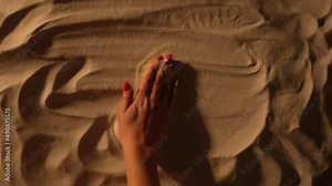 A woman's hand smoothes the sandy surface and writes sos. A call for help written on the sand of a beach. Close up of female hand is drawing inscription help. Summer holiday by the sea. Slow motion.