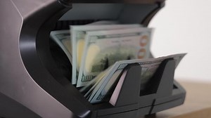 Money counter machine counting stack of US dollars, close-up on cash flow and financial operations