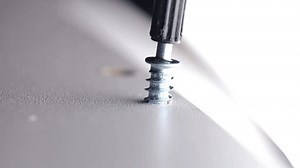 Screwing in a screw close-up. Furniture assembly stage. Macro shot of a screw and a drill. The drill screws a metal screw into a wooden board.construction and carpentry work. 4k footage
