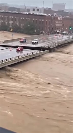 Jane Hodges on Instagram: "Shocking moment of a bridge collapse during a severe flood in the city. The video is shot from a height, showing the power of the elements and the sudden collapse of the engineering structure. Fast, muddy water with foam and debris literally swallows part of the bridge, exposing its destruction. Drivers manage to brake, avoiding falling into the turbulent river. A crowd gathers on the other bank, watching the unfolding catastrophe. Realistic footage, shot on a smartpho