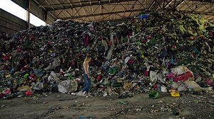 Side view: Young woman in jeans walking inside trash sorting facility
