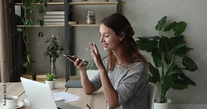 Focused young 30s woman sitting at desk at home office, dictating audio message in mobile application, enjoying distant communication, recording voice answer, activating ai assistant, web surfing. Stock Video