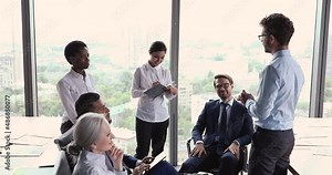 Young man psychologist coach lead motivation training seminar in diverse business people group. Multiracial corporate staff of different age gender engaged in teambuilding activity at office workplace